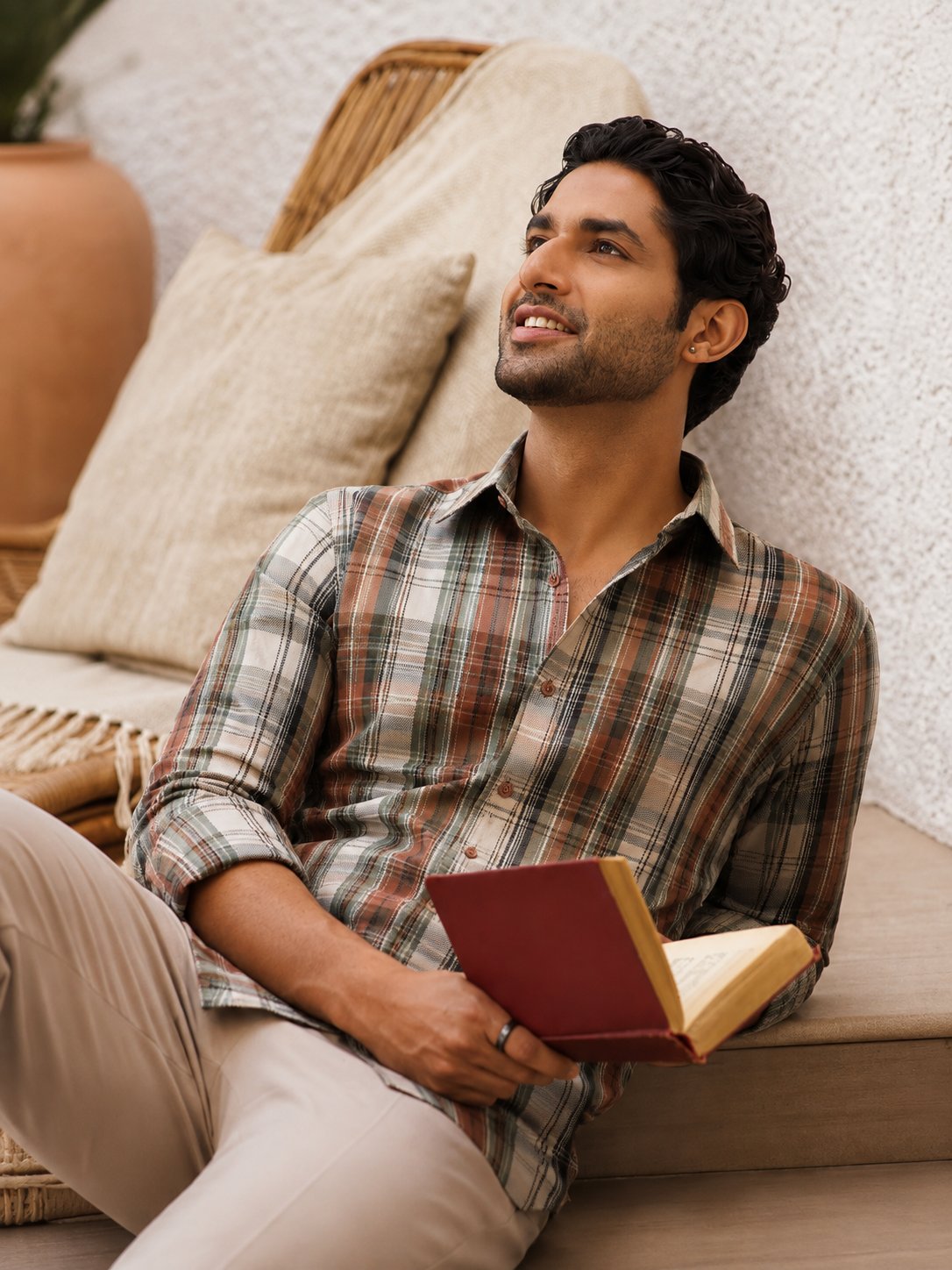 Model wearing a Yarn to Yards earth-tone check shirt, seated outdoors, reading